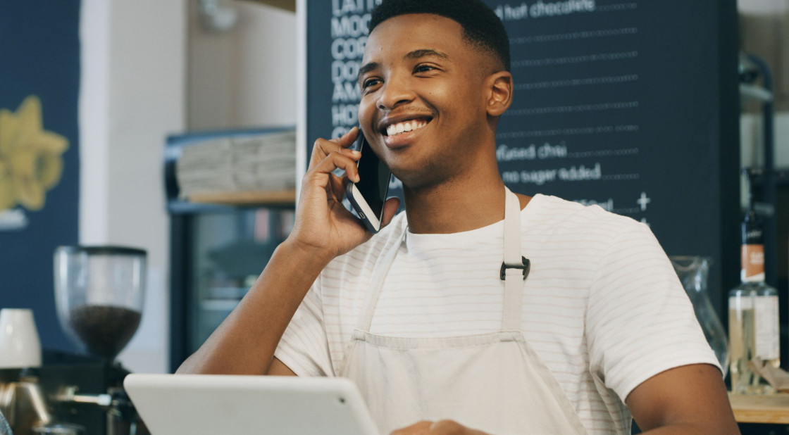 Smiling young man at cafe taking phone orders in vibrant coffee shop setting.