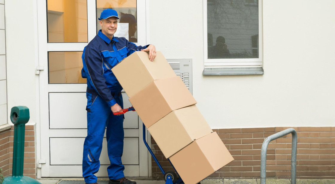 Delivery worker in blue uniform handling packages at a building entrance.
