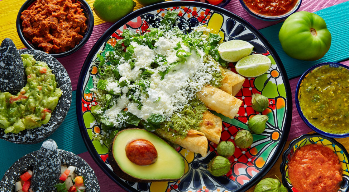 Colorful Mexican flautas with salsas, guacamole, and fresh garnishes on a vibrant table.