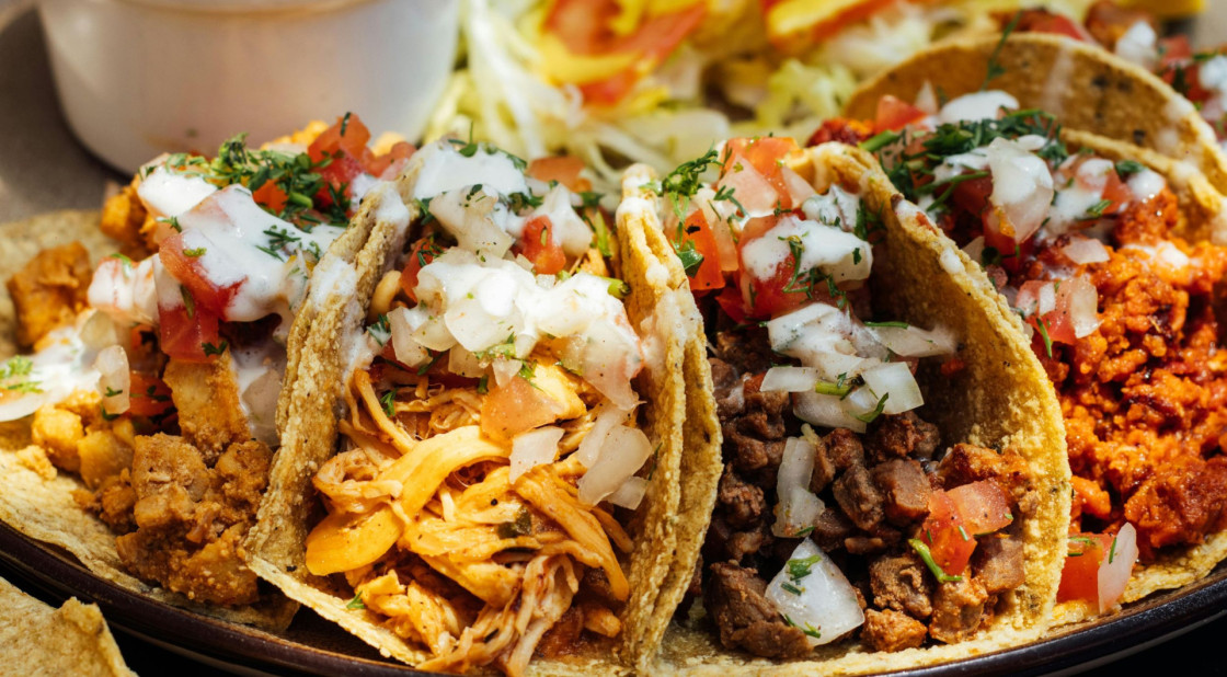 Colorful tacos with various fillings and toppings on a dark plate, showcasing Mexican cuisine.